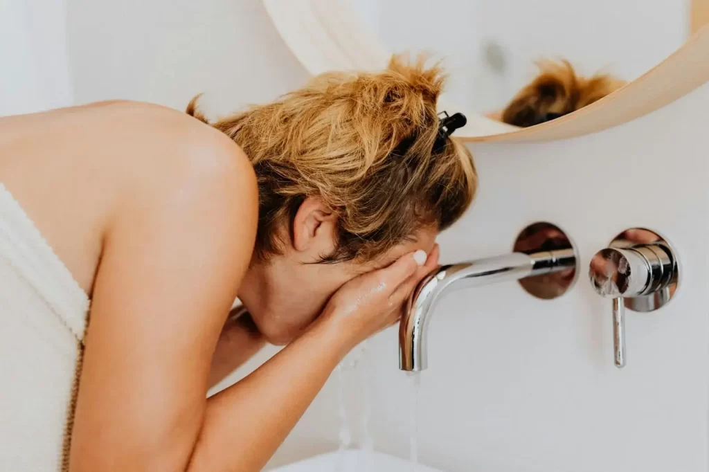 Woman washing her face on a sink with waterfall faucet